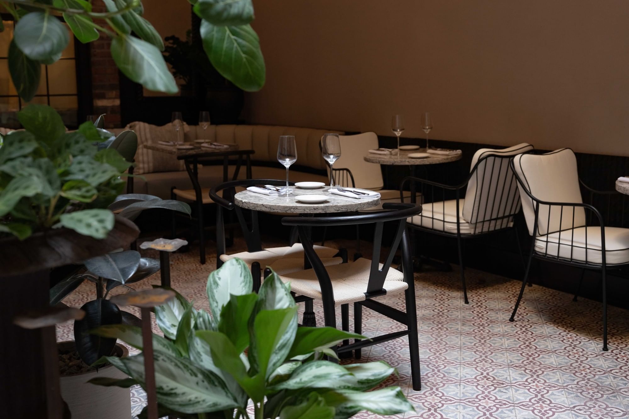 A dining area with tables and chairs, and plants in the foreground.