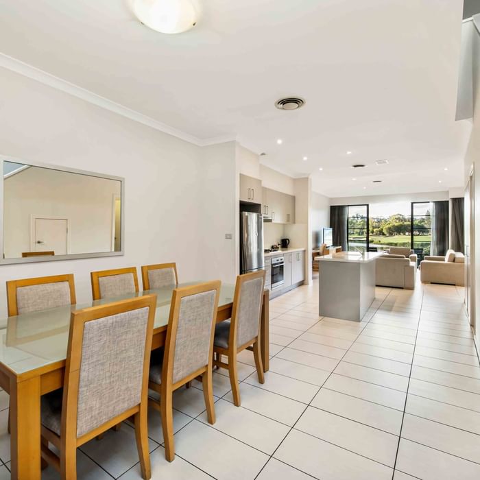 Three Bedroom Apartment dining area with table, leading to an open-plan kitchen and living area at Mercure Kooindah Waters