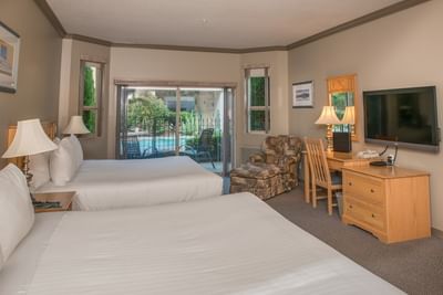 Two beds face the patio door, a lounge chair by the desk with a TV in Courtside Queen Executive at Hilltop Inn Salmon Arm
