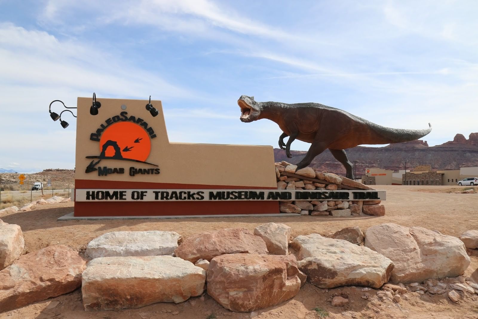 A large sign with a dinosaur statue in the desert.