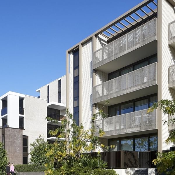 Modern apartment complex with balconies, surrounded by trees and greenery under a clear blue sky.