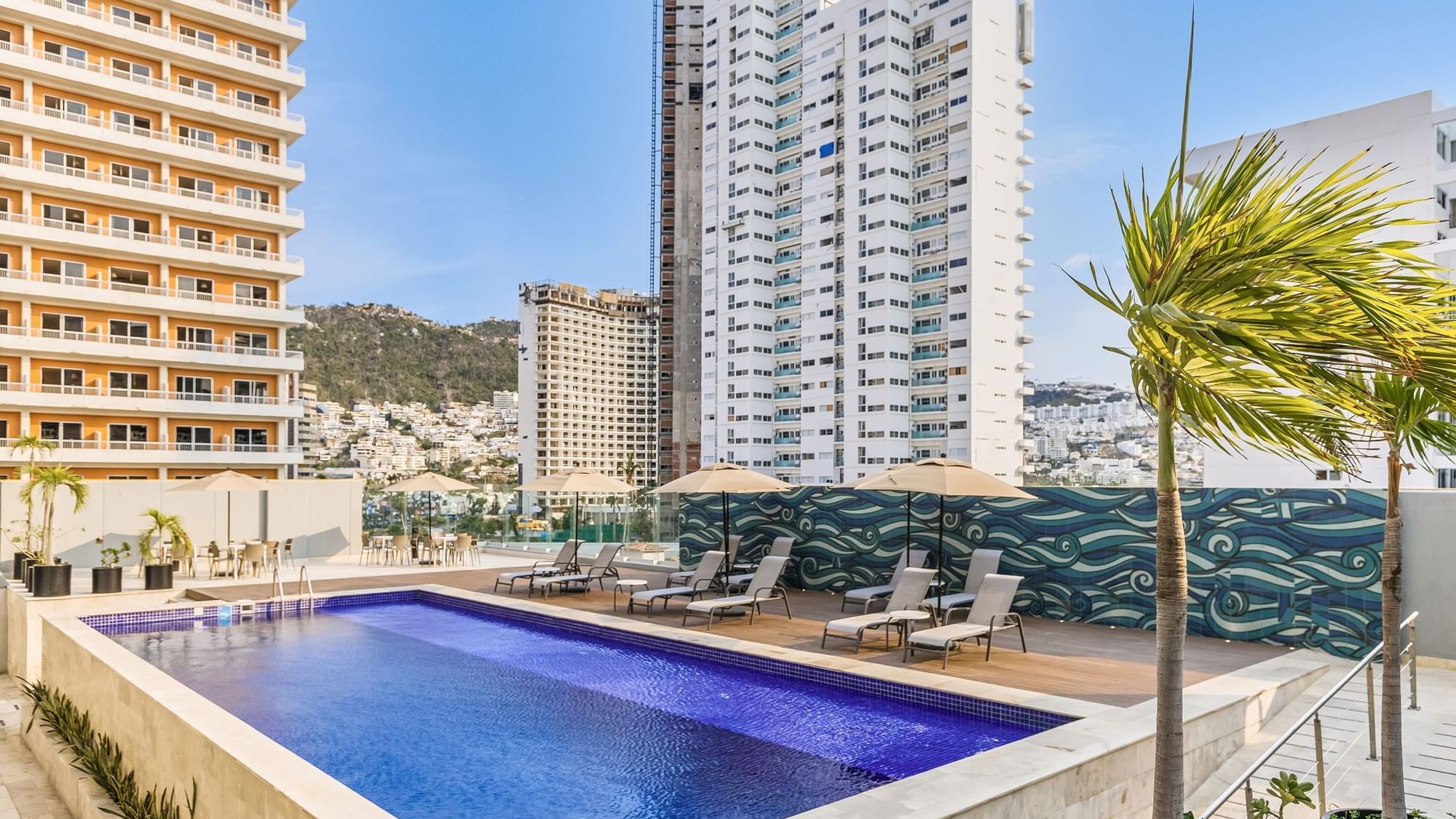 Outdoor pool area with sun loungers & patio umbrellas at One Acapulco Costera