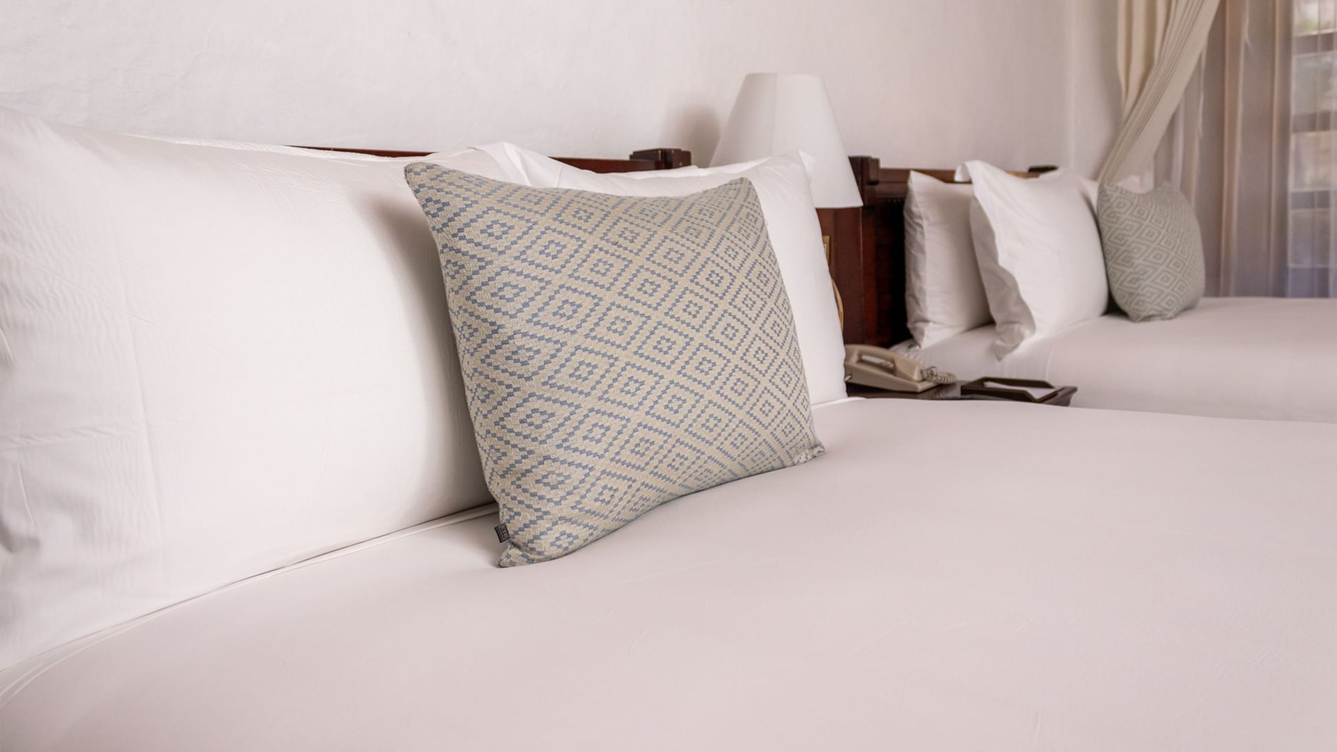 Two double beds with white linens and patterned pillows in a room at Quinta Real Oaxaca in Oaxaca de Juarez.