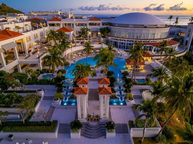 Aerial view of El Conquistador Resort with a pool, palm trees, ornate fountains, and modern architecture at sunset