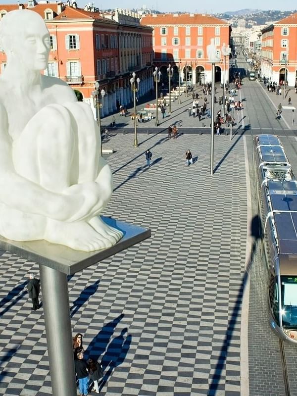 Modern tram passing by a public square with a white statue sculpture in the city near Splendid Hotel & Spa Nice