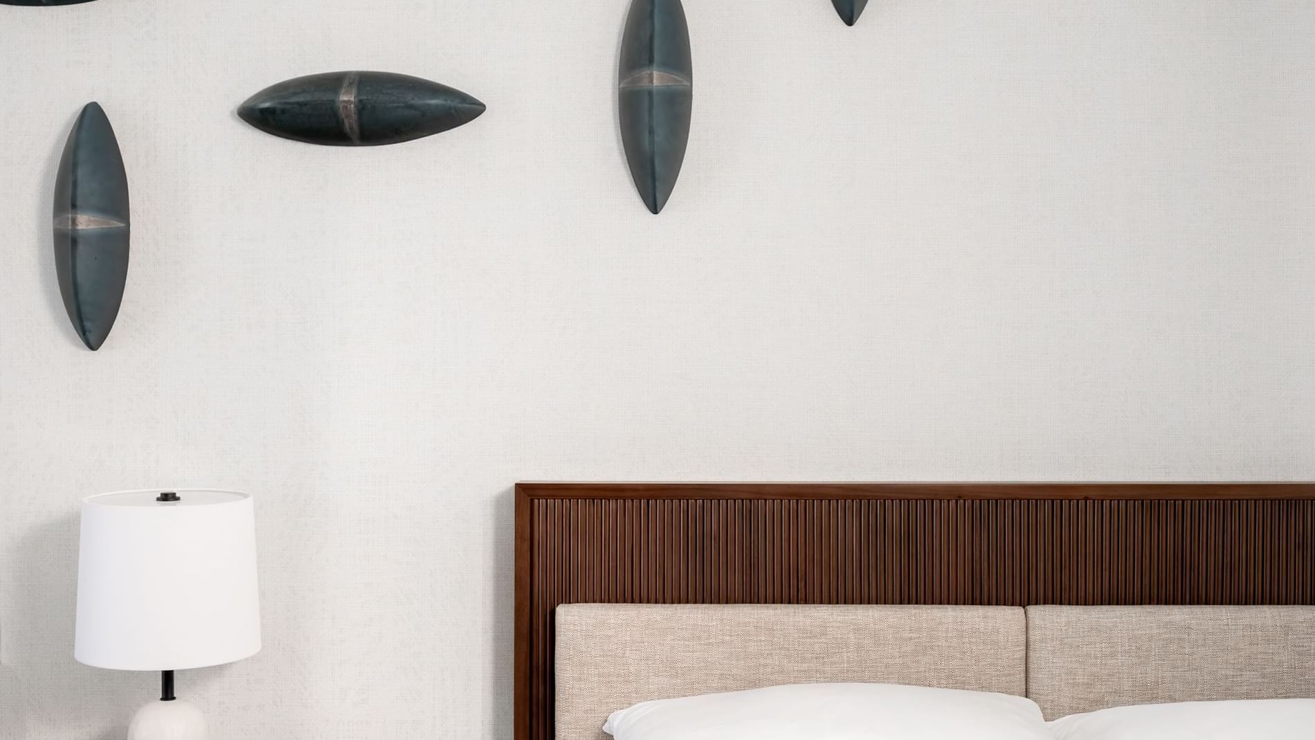 A partial view of a hotel room with a bed, lamp, and surfboard-inspired wall decor.