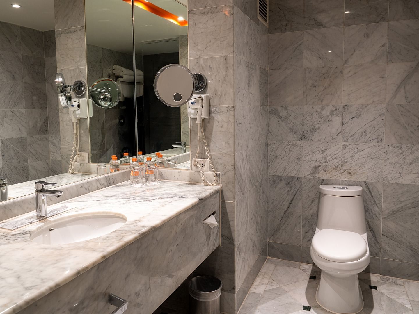 Bathroom with a large vanity mirror, white commode, and bright lighting in the King Deluxe Room at Real Inn Tijuana