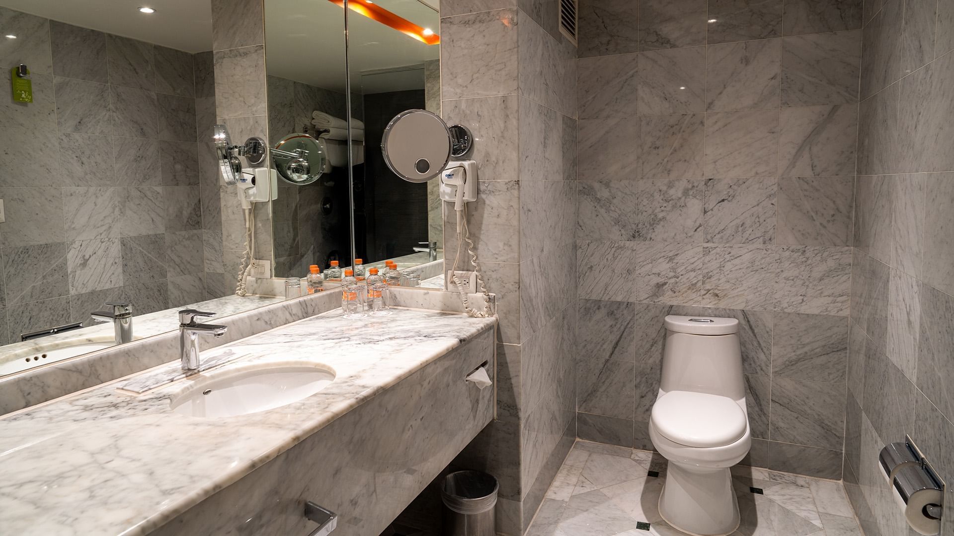 Bathroom with a large vanity mirror, white commode, and bright lighting in the King Deluxe Room at Real Inn Tijuana