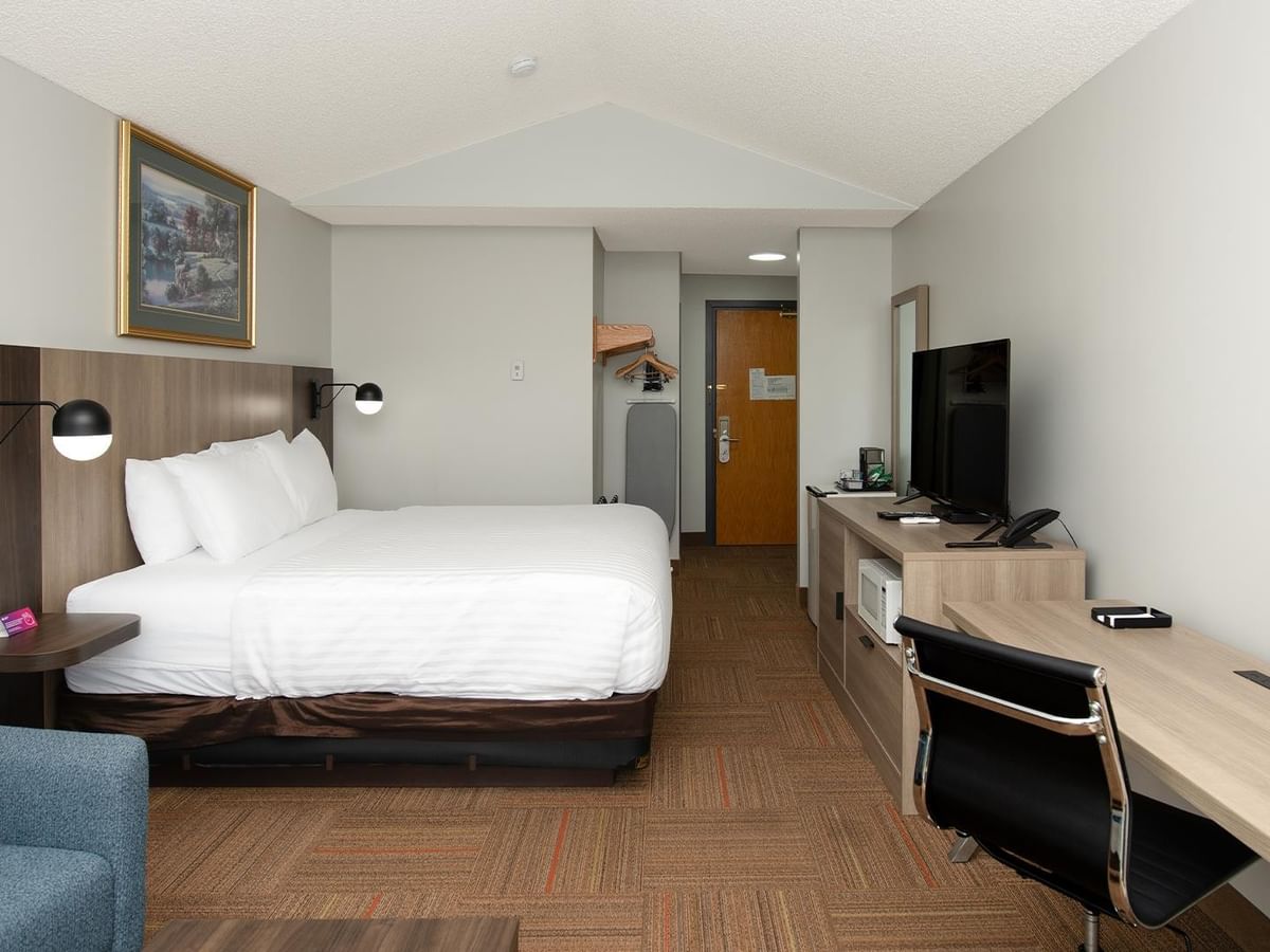 Coast King room with white bedding, wood headboard, work desk, and wall-mounted TV.