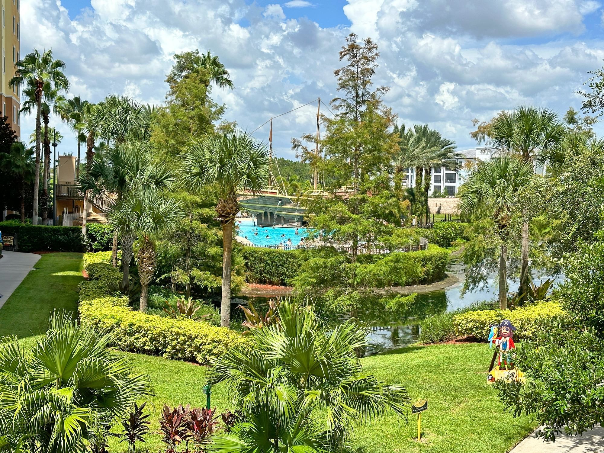 A tropical resort landscape with a pool, pond, and lush greenery.