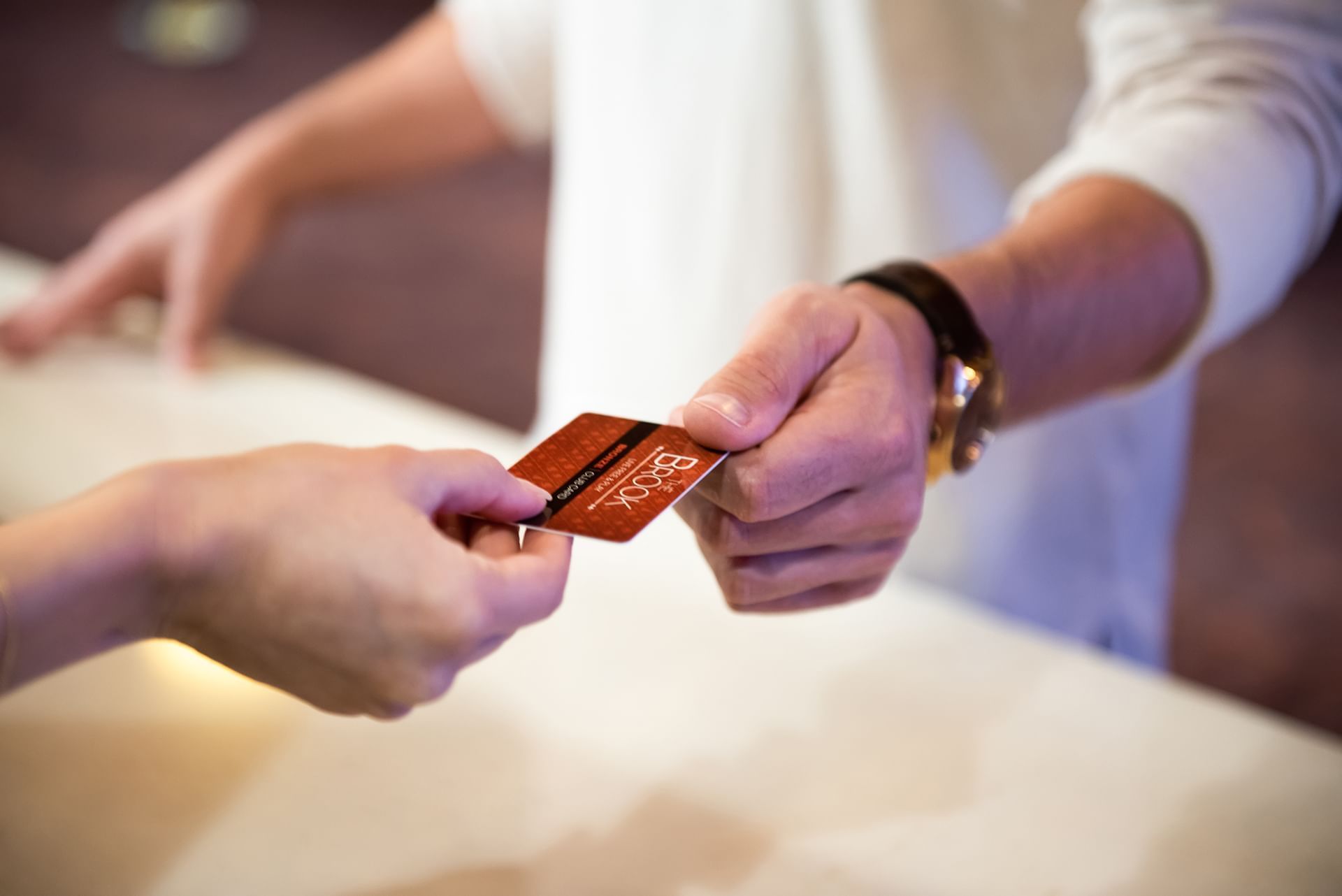 Guest hands The Brook rewards card to a staff member across a white reception counter under soft light at The Brook