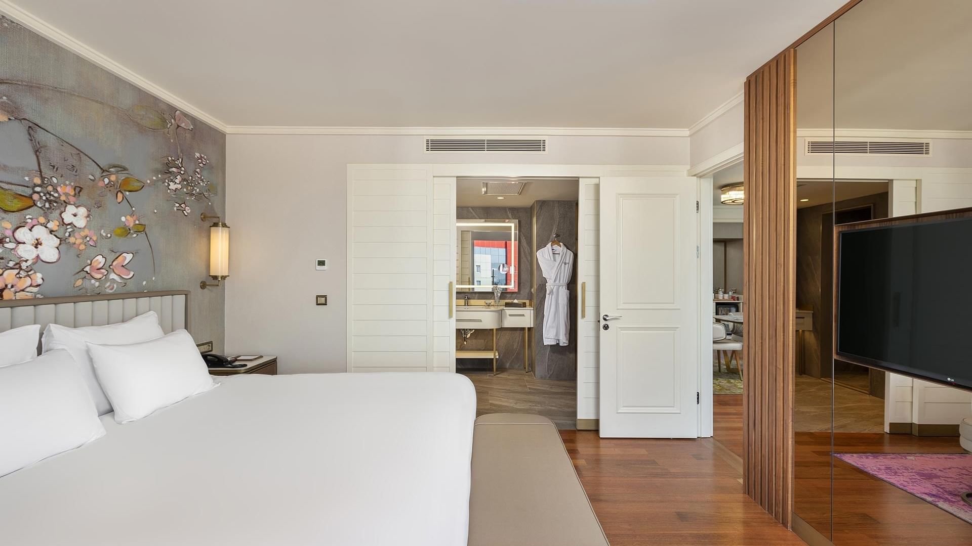 Titanic Port Bakırköy'de, büyük bir yatak, çiçekli duvar sanatı, banyo ve ahşap zemin üzerinde bir TV seti bulunan Suite oda.