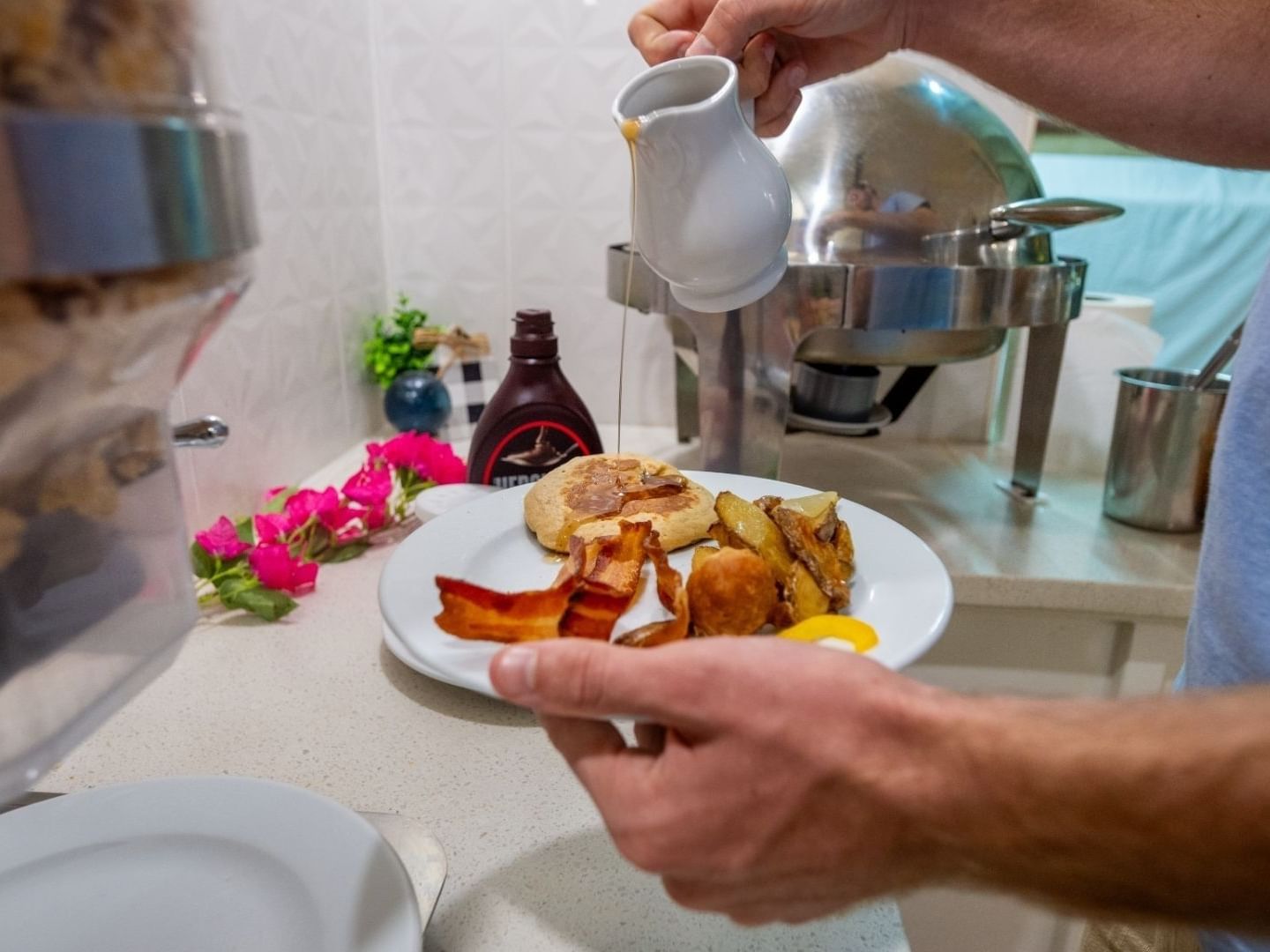 Person pouring syrup onto breakfast plate with eggs and bacon at Savannah Beach Hotel.