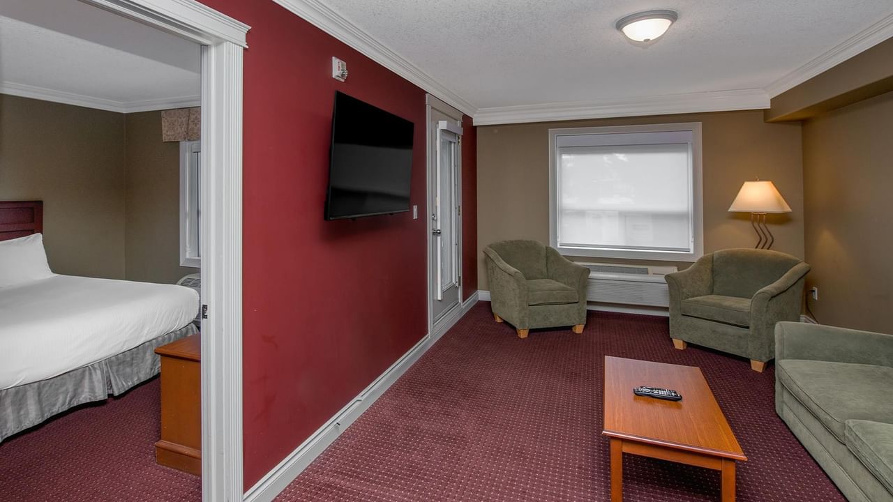 Coast Edson Hotel suite with separate bedroom, red accent wall, flat-screen TV, and sage green seating area.