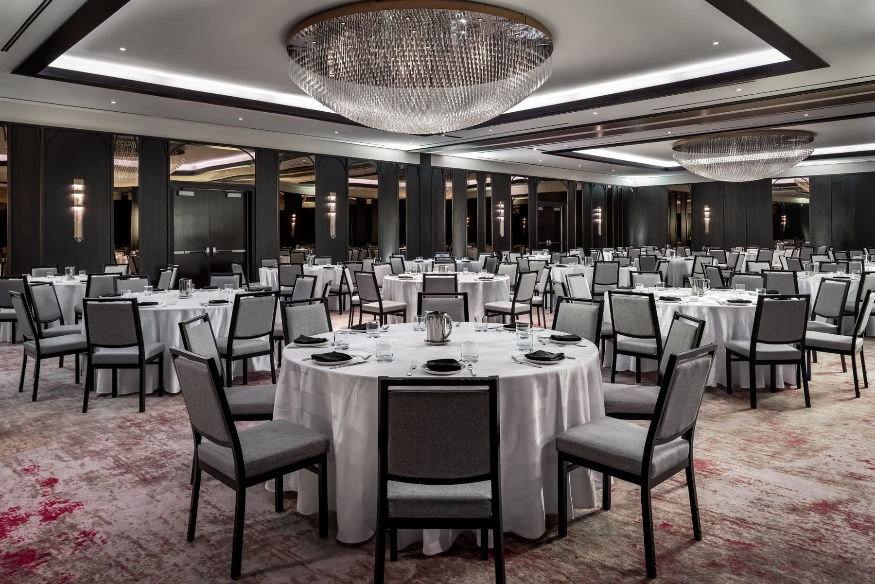 Princes\' Gates Ballroom with round dining tables and crystal chandelier between dark wood accents at Hotel X Toronto