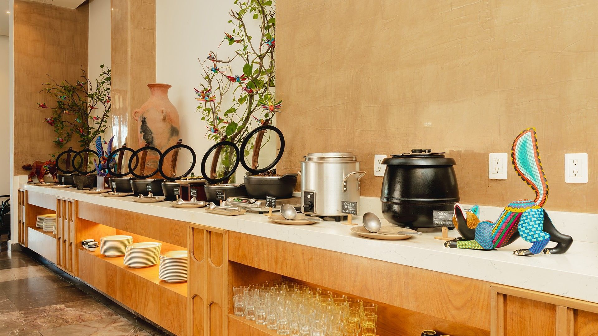 Luxurious buffet setup with ceramic pots, vibrant decorations, & lush greenery in Chez Binni at Camino Real Zaashila Huatulco