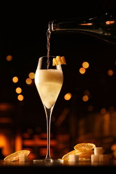Person pouring sparkling drink into glass garnished with lemon slices in Square One at Park Hyatt Saigon