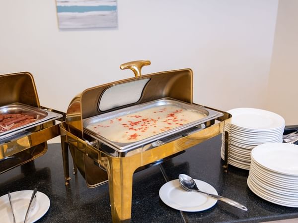 Buffet spread with chafing dishes and stack of plates at Saja by Warwick Makkah.
