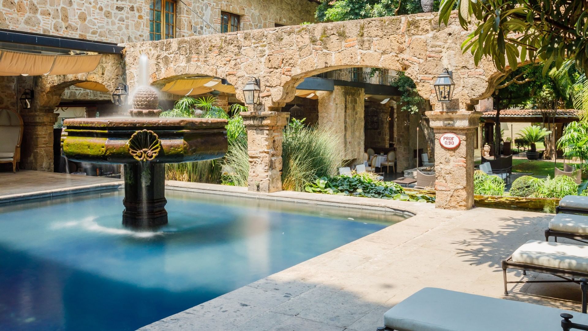 Outdoor pool area with a stone fountain and white lounge chairs at Quinta Real Guadalajara