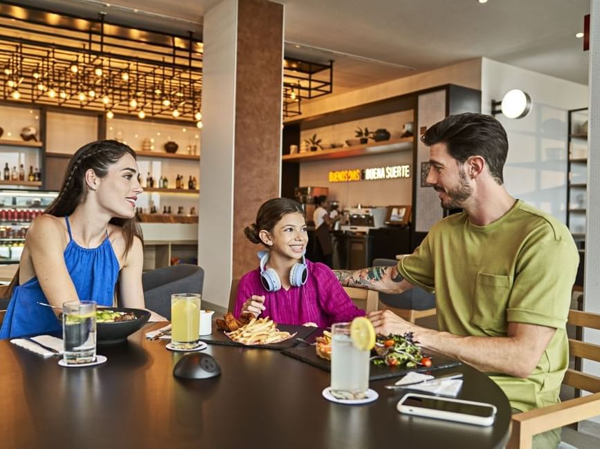 A family sitting at a dining table with a variety of food & juice for breakfast at IOH Hotels