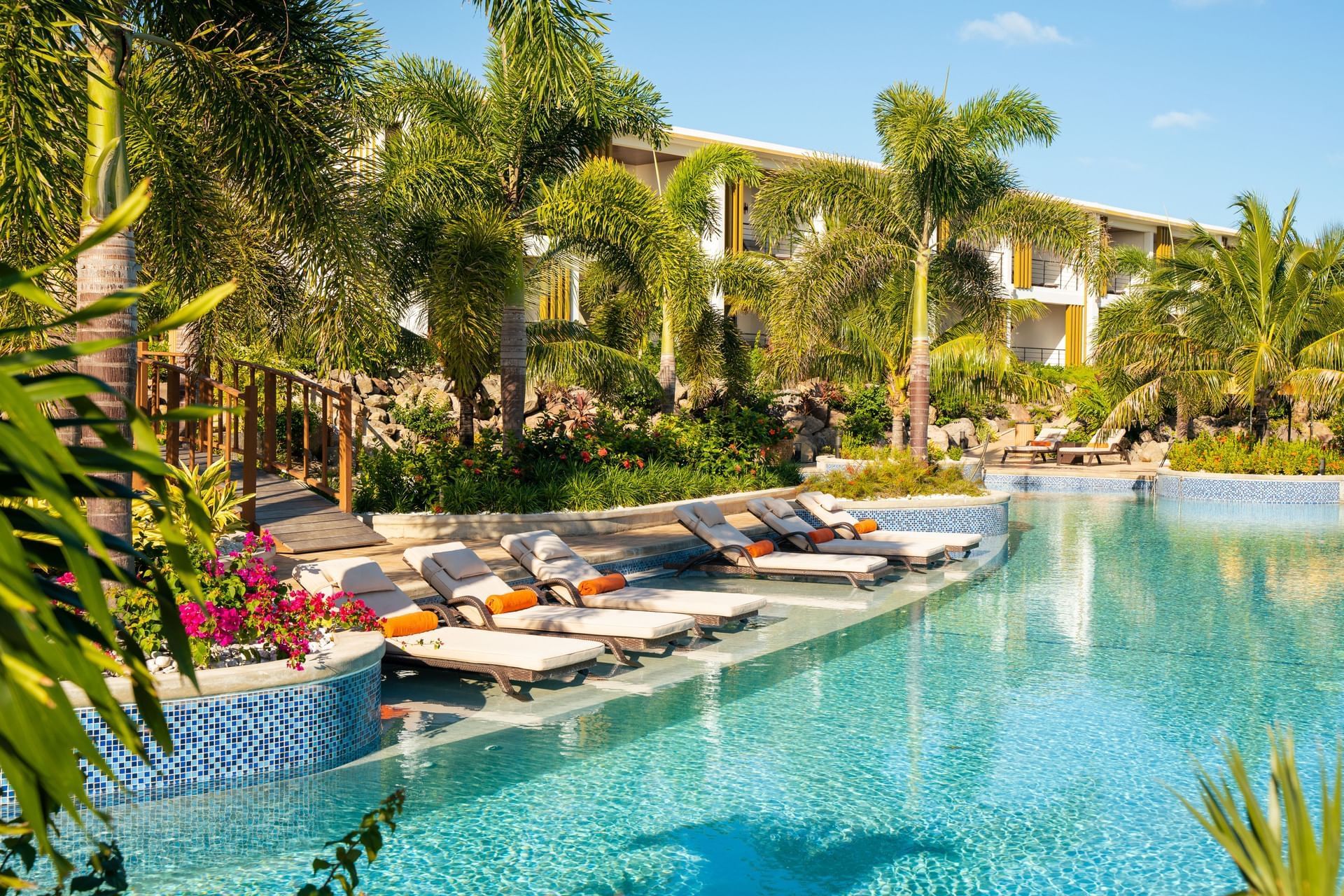 Hummingbird pool surrounded by lush palm trees and colorful flowers, with lounge chairs at Golden Rock Resort