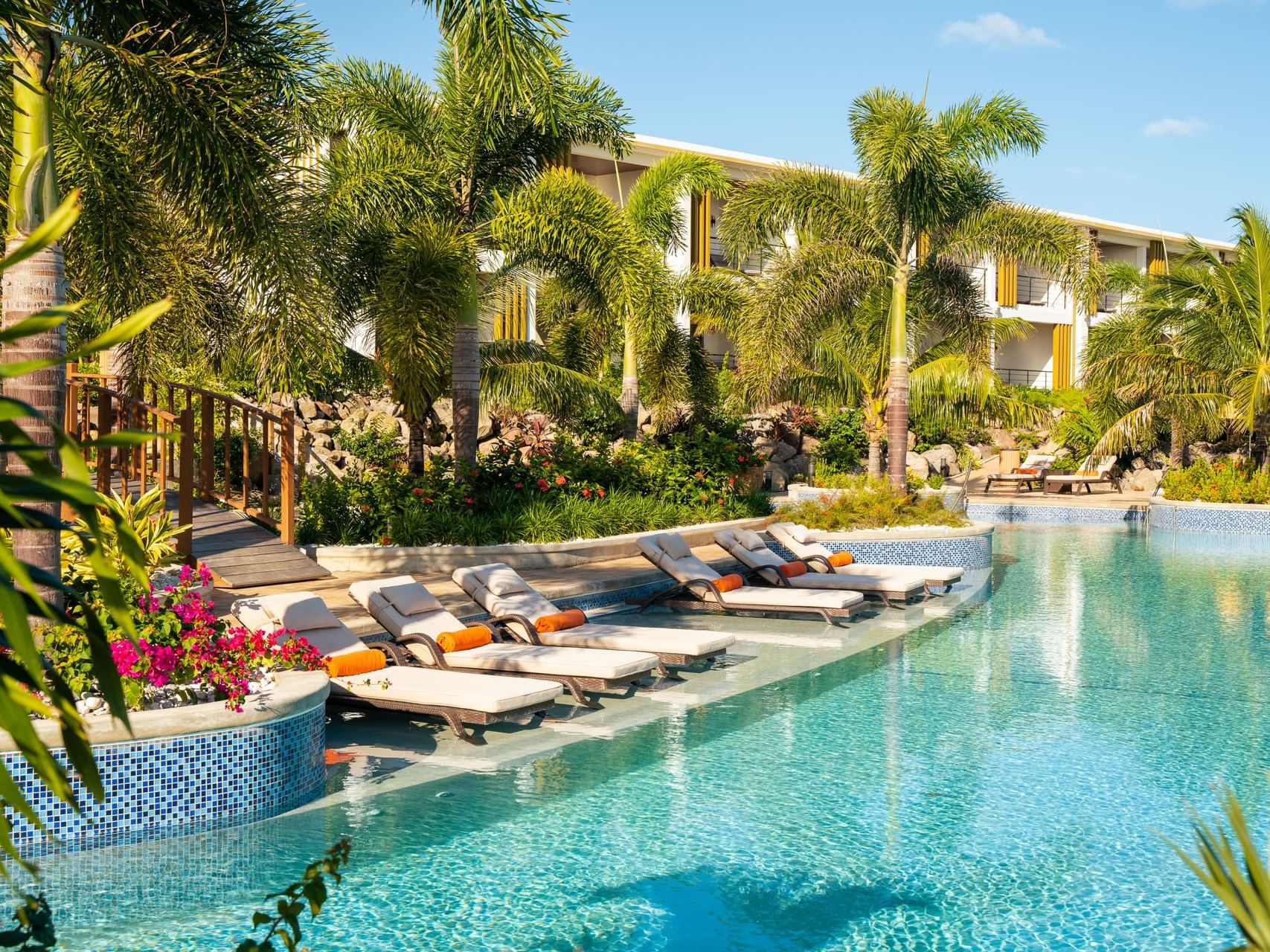 Hummingbird pool surrounded by lush palm trees and colorful flowers, with lounge chairs at Golden Rock Resort