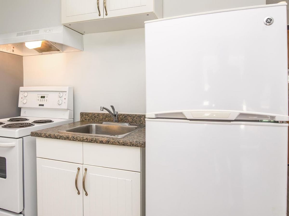 Compact kitchenette with white appliances, granite countertop and stainless sink.