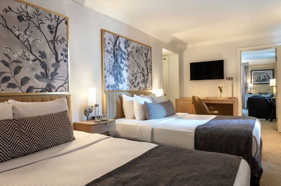 Beds with a side table near work desk under a hanging TV in Executive Two Queen Beds at Warwick Allerton Chicago