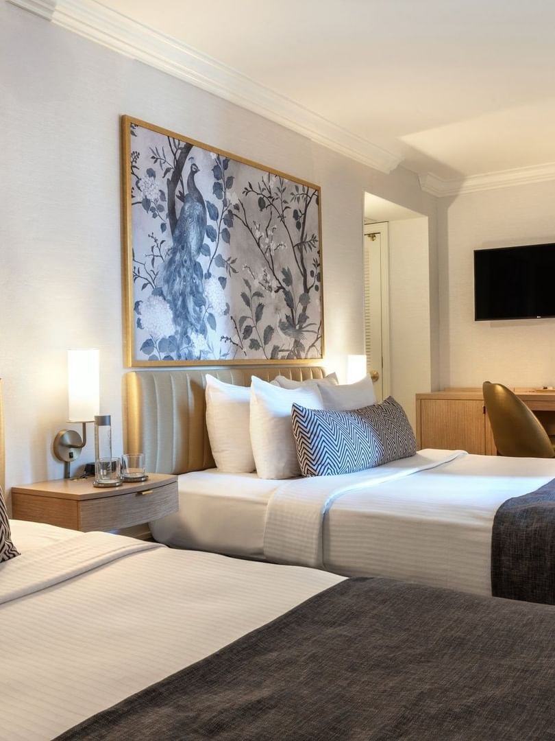 Beds with a side table near work desk under a hanging TV in Executive Two Queen Beds at Warwick Allerton Chicago