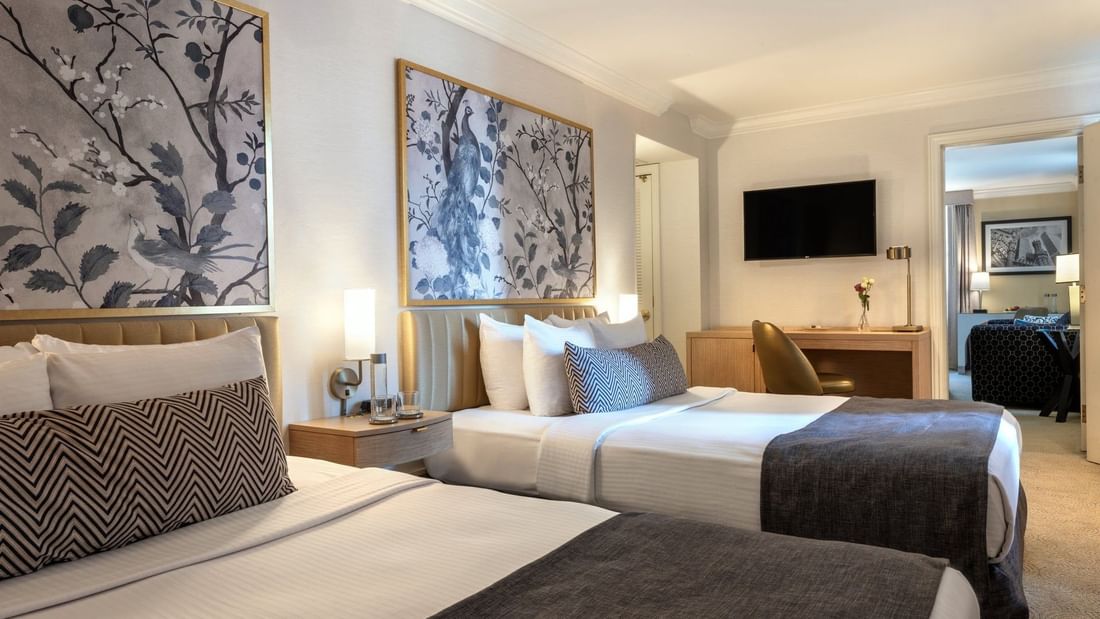 Beds with a side table near work desk under a hanging TV in Executive Two Queen Beds at Warwick Allerton Chicago