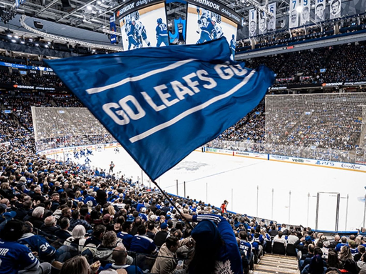 Fans holding a GO LEAFS GO flag above their heads by Scotiabank Arena near Hotel X Toronto