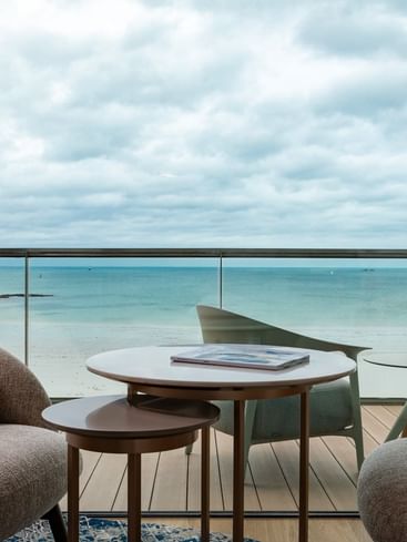 Relaxed balcony seating with armchairs and coffee table, overlooking the ocean under a cloudy sky at Oceania Saint-Malo