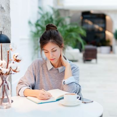 A girl writing while having a cup of coffee at Originals Hotels