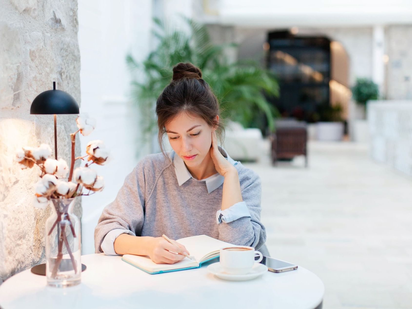 A girl writing while having a cup of coffee at Originals Hotels