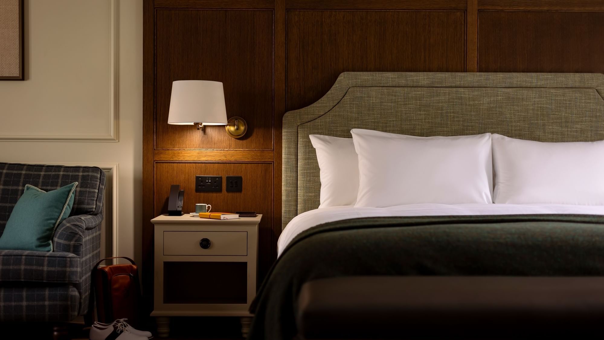 Courtyard Suite with a plush bed, a nightstand with a lamp, and a plaid chair at Dunluce Lodge