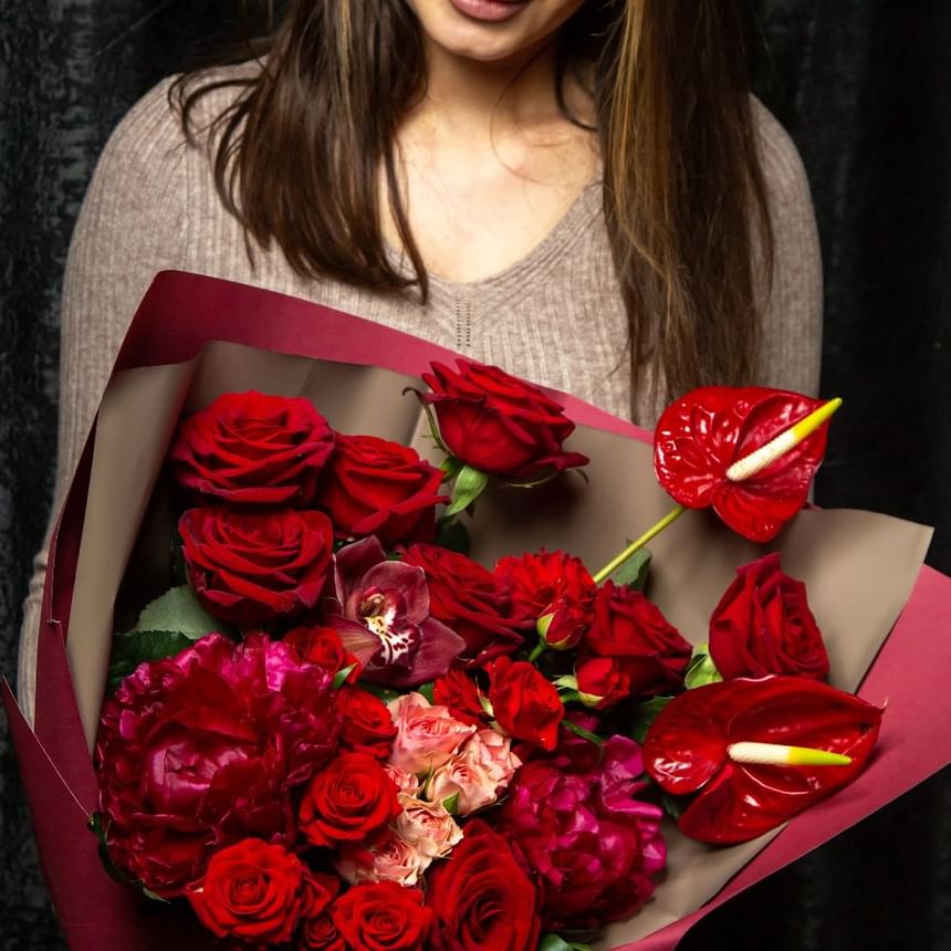 Mujer sostiene un frondoso ramo de rosas rojas, orquídeas y flores rosas envuelto en papel en Megapolis Hotel Panama