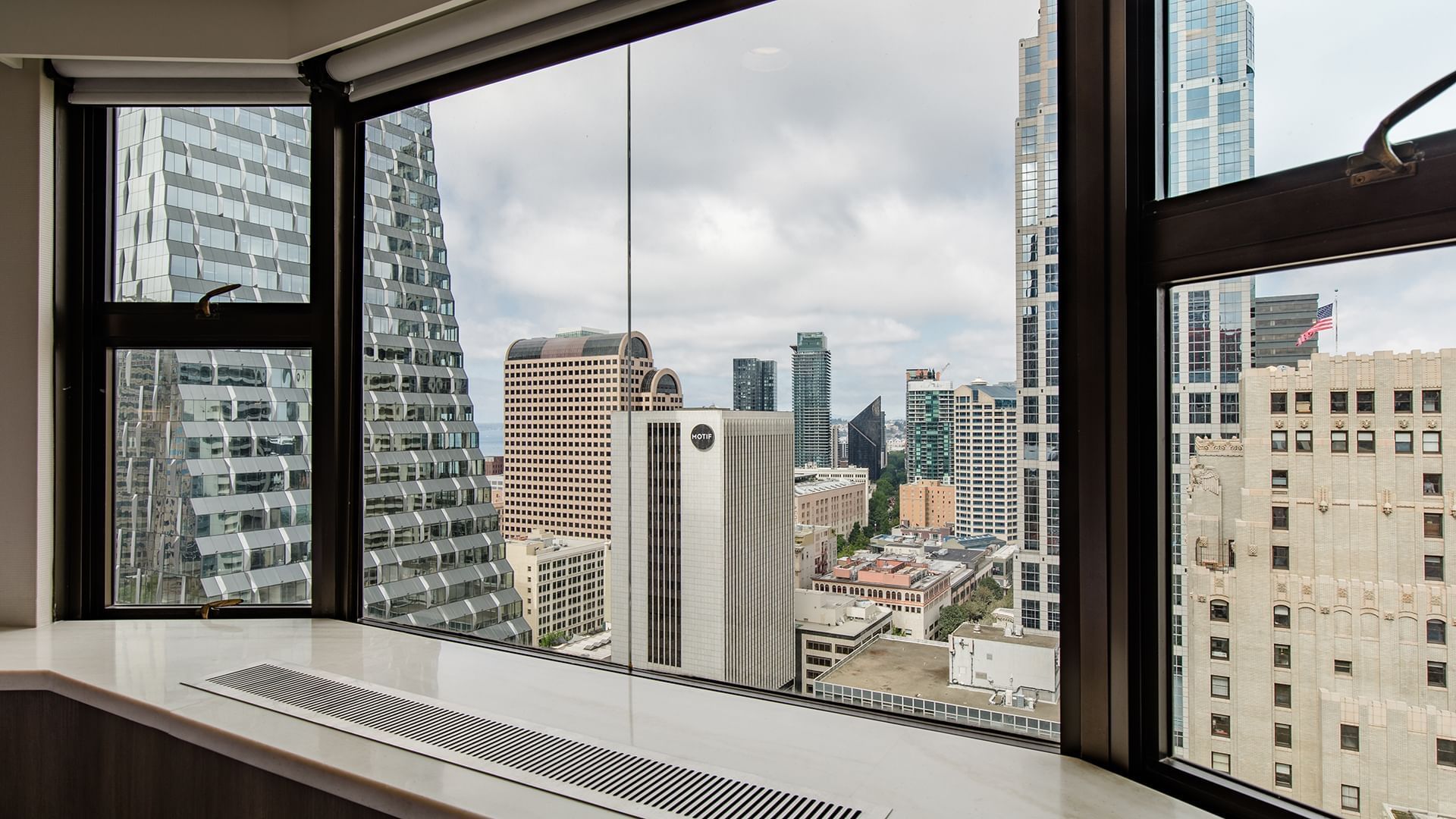 A city view from a hotel room window showing high-rise buildings under a cloudy sky.