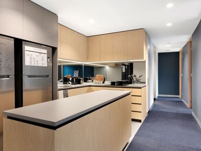 Modern kitchen with wooden cabinets, stainless steel appliances, and a breakfast bar at La Trobe University - North and South Apartments.