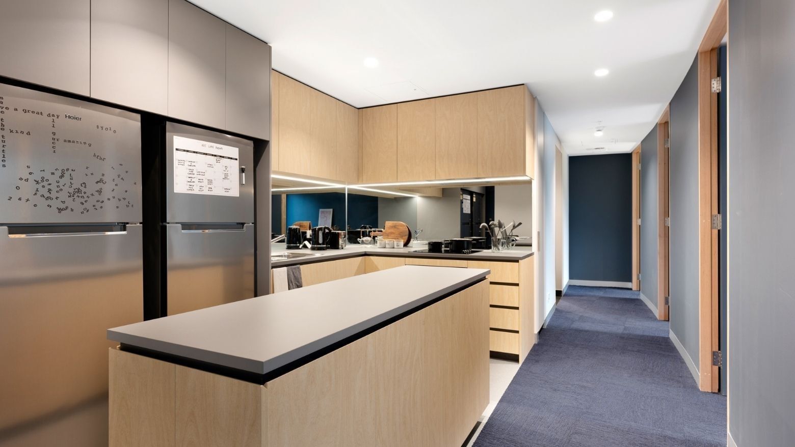 Modern kitchen with wooden cabinets, stainless steel appliances, and a breakfast bar at La Trobe University - North and South Apartments.