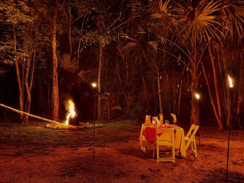 Romantic dinner table arranged by trees & a firepit at night in The Explorean Kohunlich