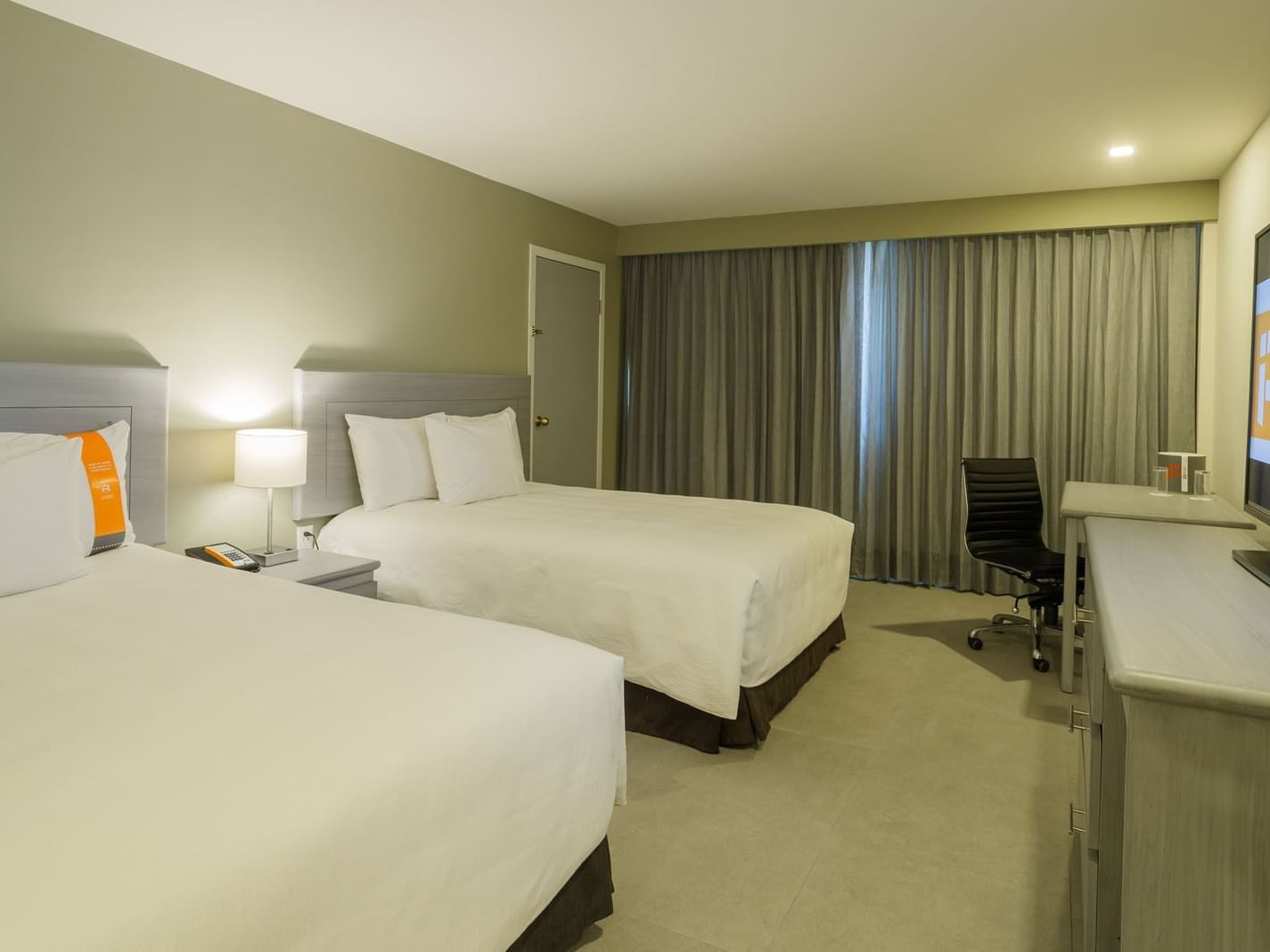 2 Double Deluxe room with white linens, a sleek black desk chair, and grey blackout curtains at Real Inn Mexicali