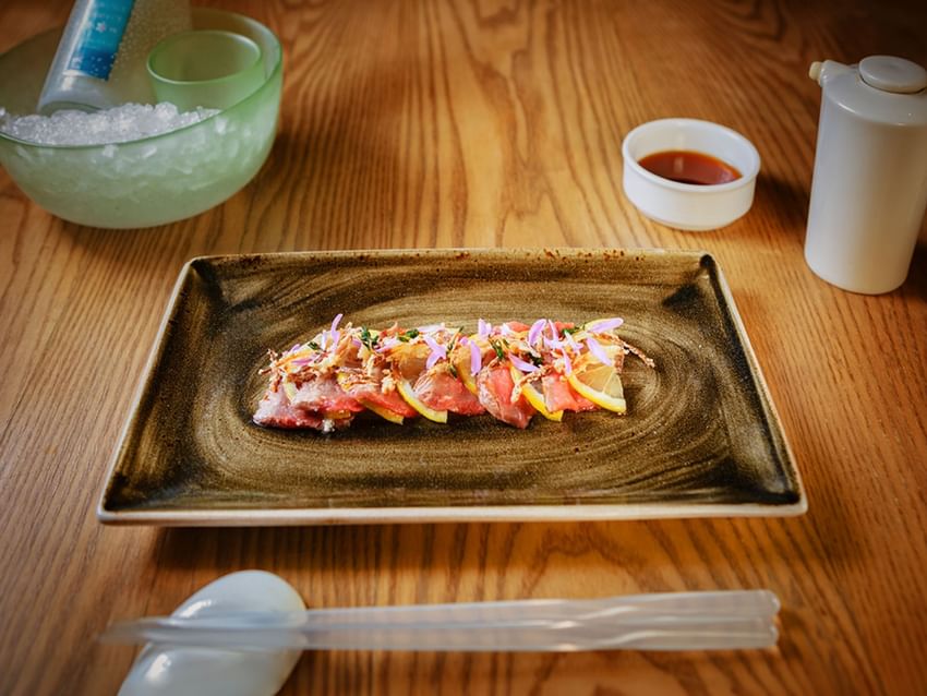 Sliced meat appetizer with lemon and flower garnish on a tray at Camino Real Hotels