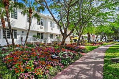 Bright exterior view of the Tradewinds Apartment Hotel building surrounded by lush tropical landscaping and vibrant flowers