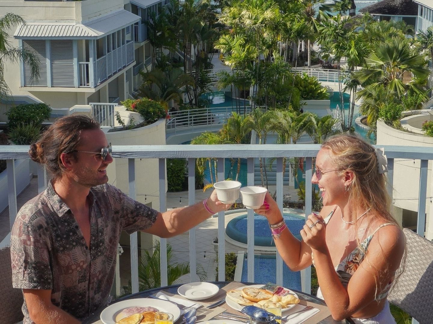 Two people enjoy a meal on a balcony overlooking a swimming pool at Savannah Beach Hotel.