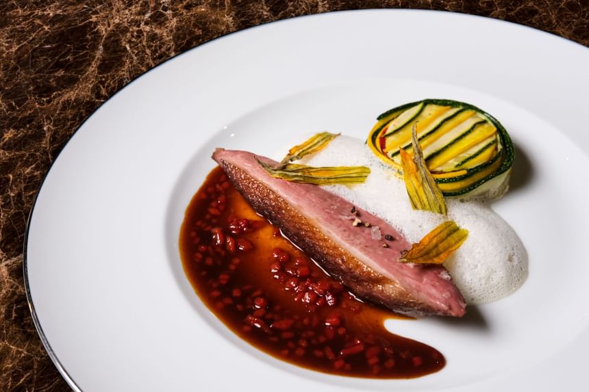 Dish with a seared duck breast, vibrant sauce, zucchini ribbons, & a textured foam served in Square One at Park Hyatt Saigon