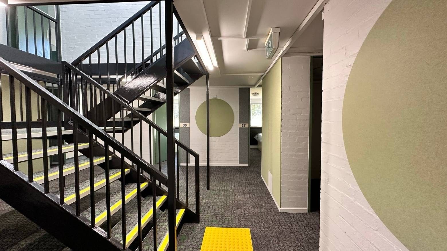 Modern staircase with yellow tactile strips and green walls at La Trobe University – Menzies College.