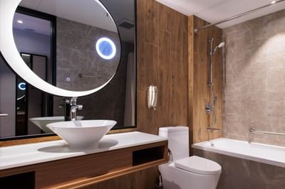 Park Hotel Hong Kong Superior Room bathroom with mirror, white sink, wooden cabinet, toilet, and bathtub with a showerhead.