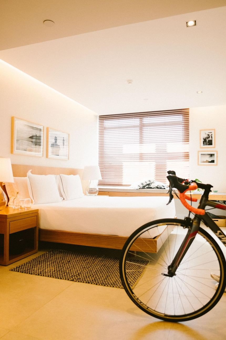 Interior de um quarto no Janeiro Hotel no Leblon, Rio de Janeiro, com uma bike dentro de um quarto com cama e quadros