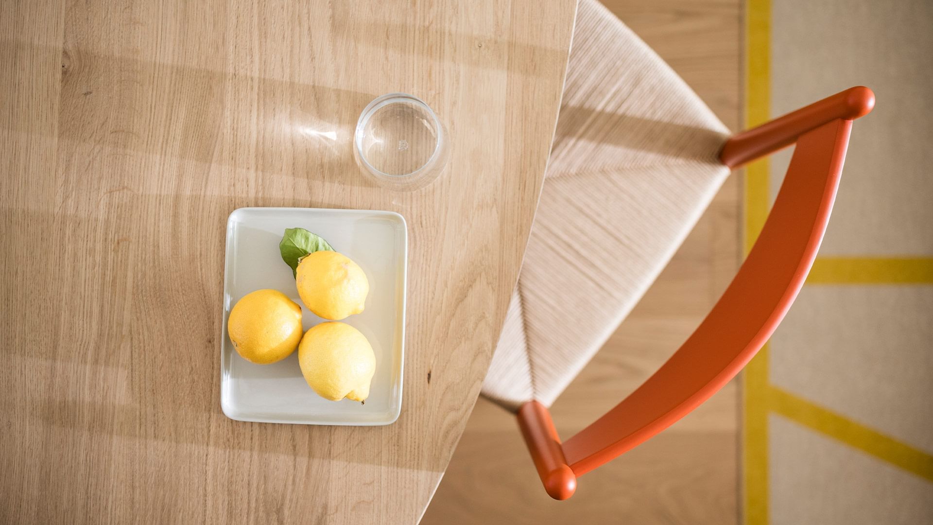 Wooden table with three lemons, a glass, and a chair with yellow lines in the background.