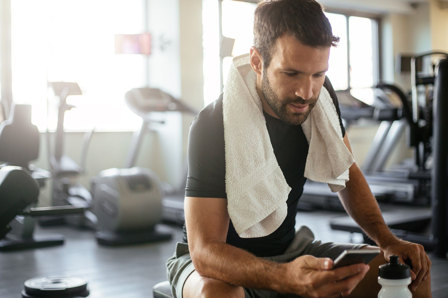 Hombre concentrado descansa entre series revisando su teléfono en el gimnasio del hotel en Fiesta Inn